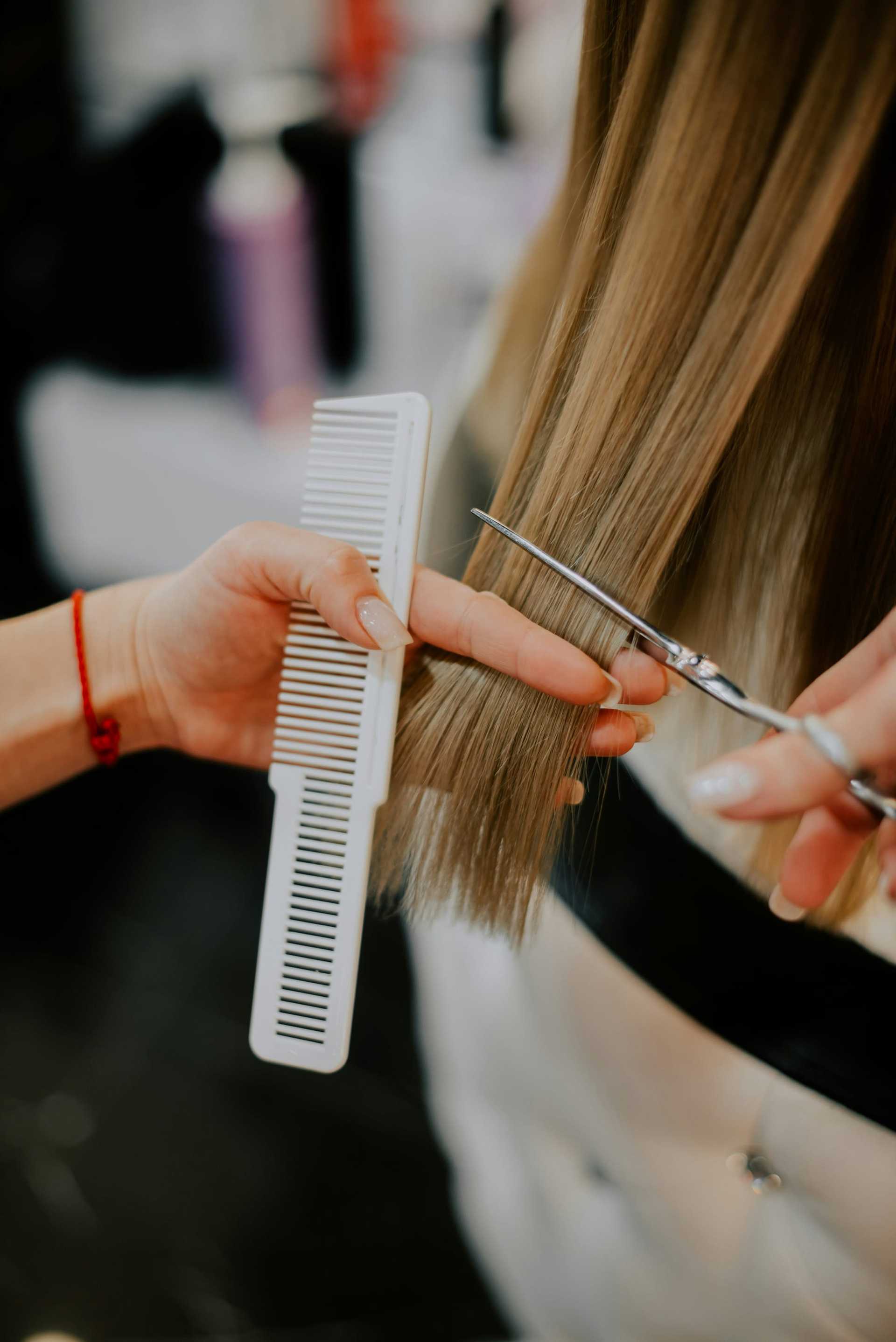 Hairdresser cutting long blonde hair with scissors and comb.