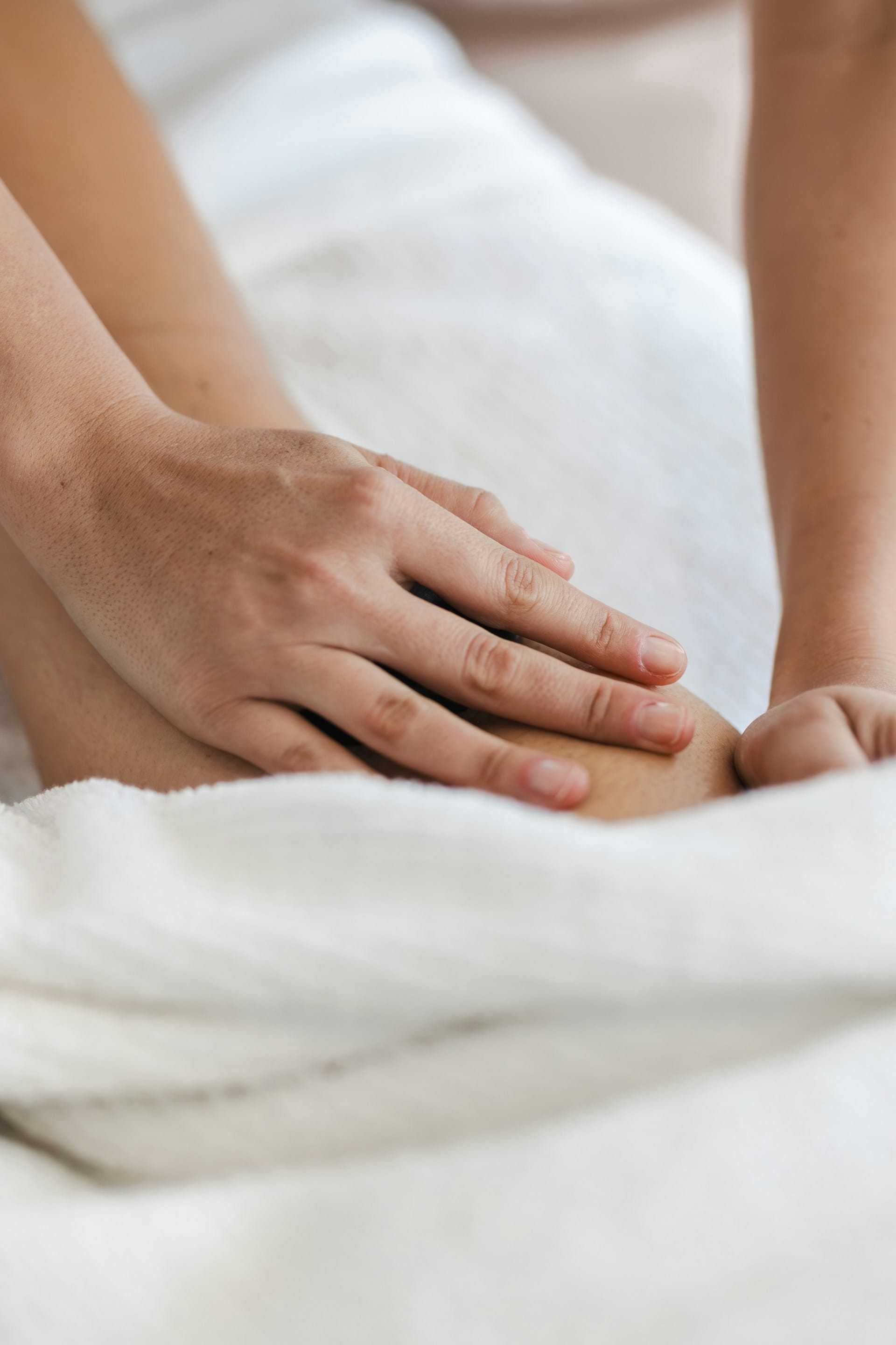 Hands massaging a leg with a white towel nearby.