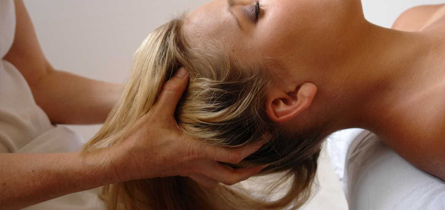 Massage therapist performing a relaxing head massage on a woman lying down.