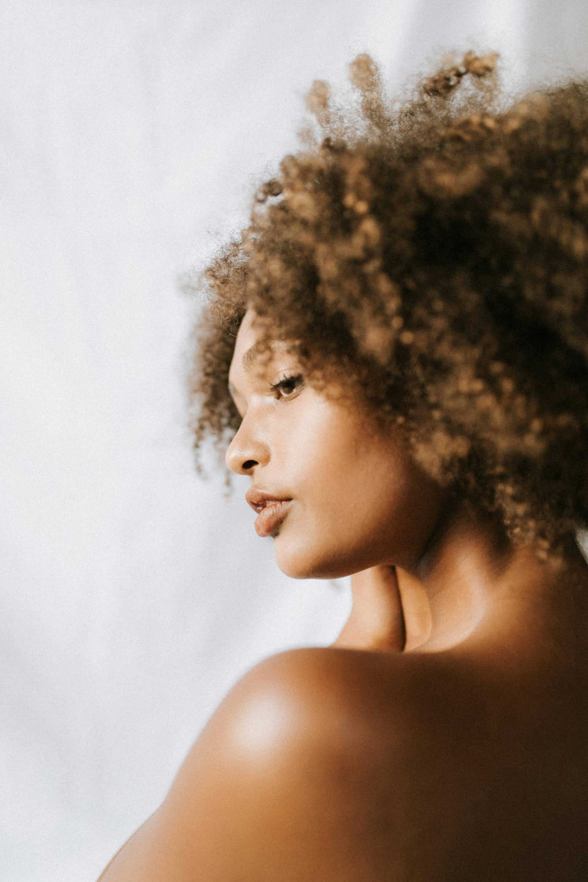 Woman with curly hair looking over shoulder against light background.