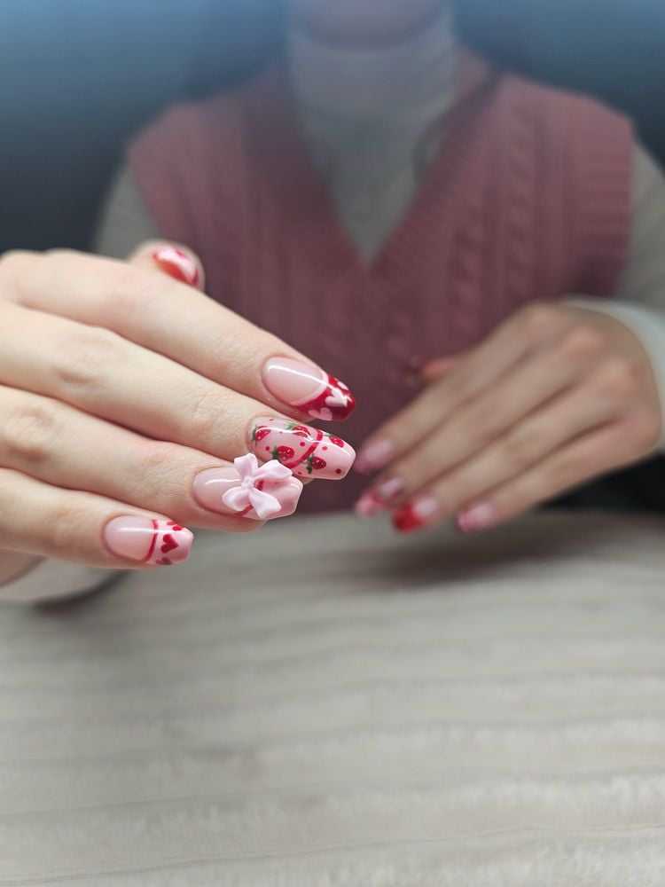 Pink nails with floral designs and a bow accent on one finger.