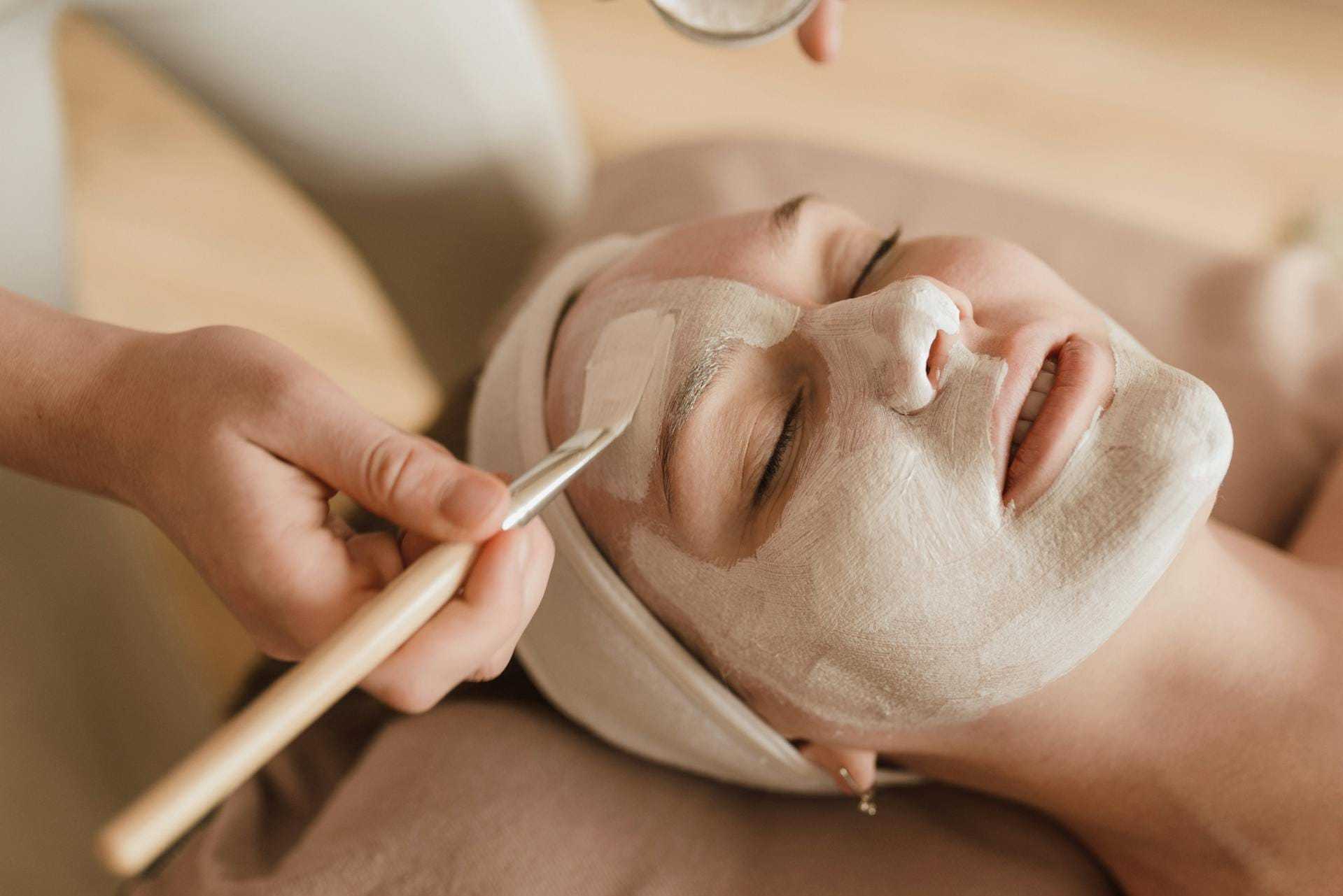 Facial treatment with cream applied by hand using a brush on a relaxed woman's face.