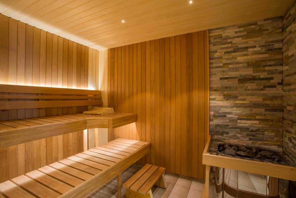 Cozy wooden sauna with stone wall and built-in heater for relaxation.