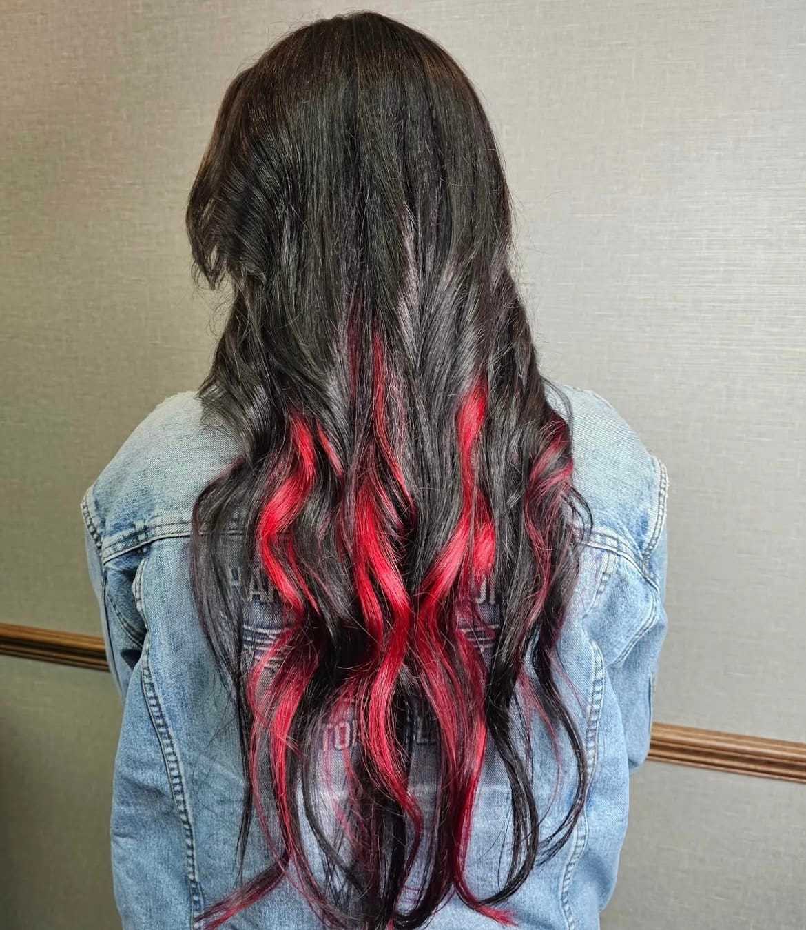 Long black hair with vibrant red highlights cascading down the back, wearing a denim jacket.