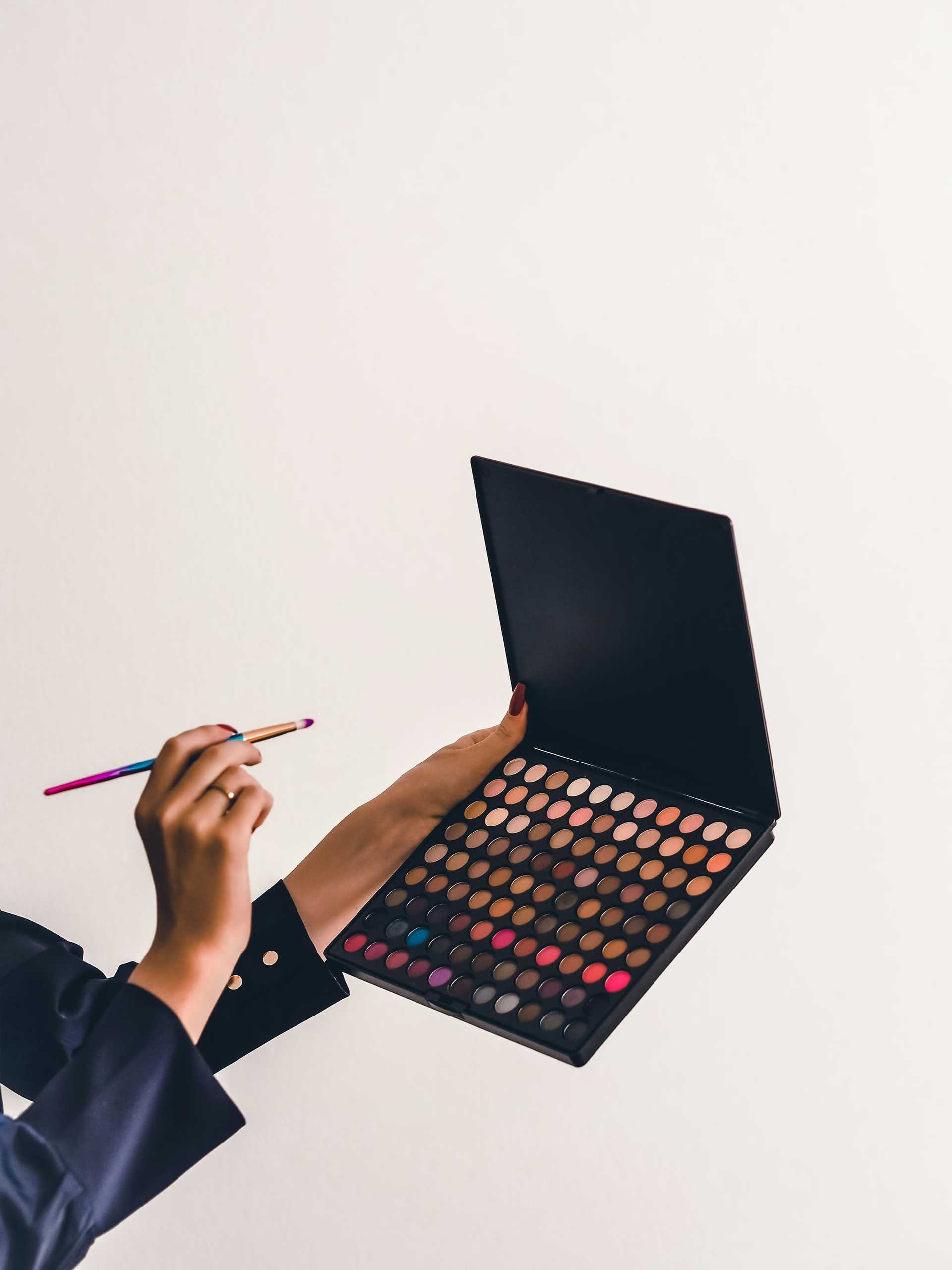 Open makeup palette with multicolored eyeshadows and a brush in hand.